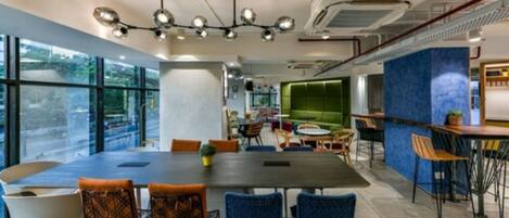 A modern dining area with a large table, blue chairs, and a green cushioned seating area.