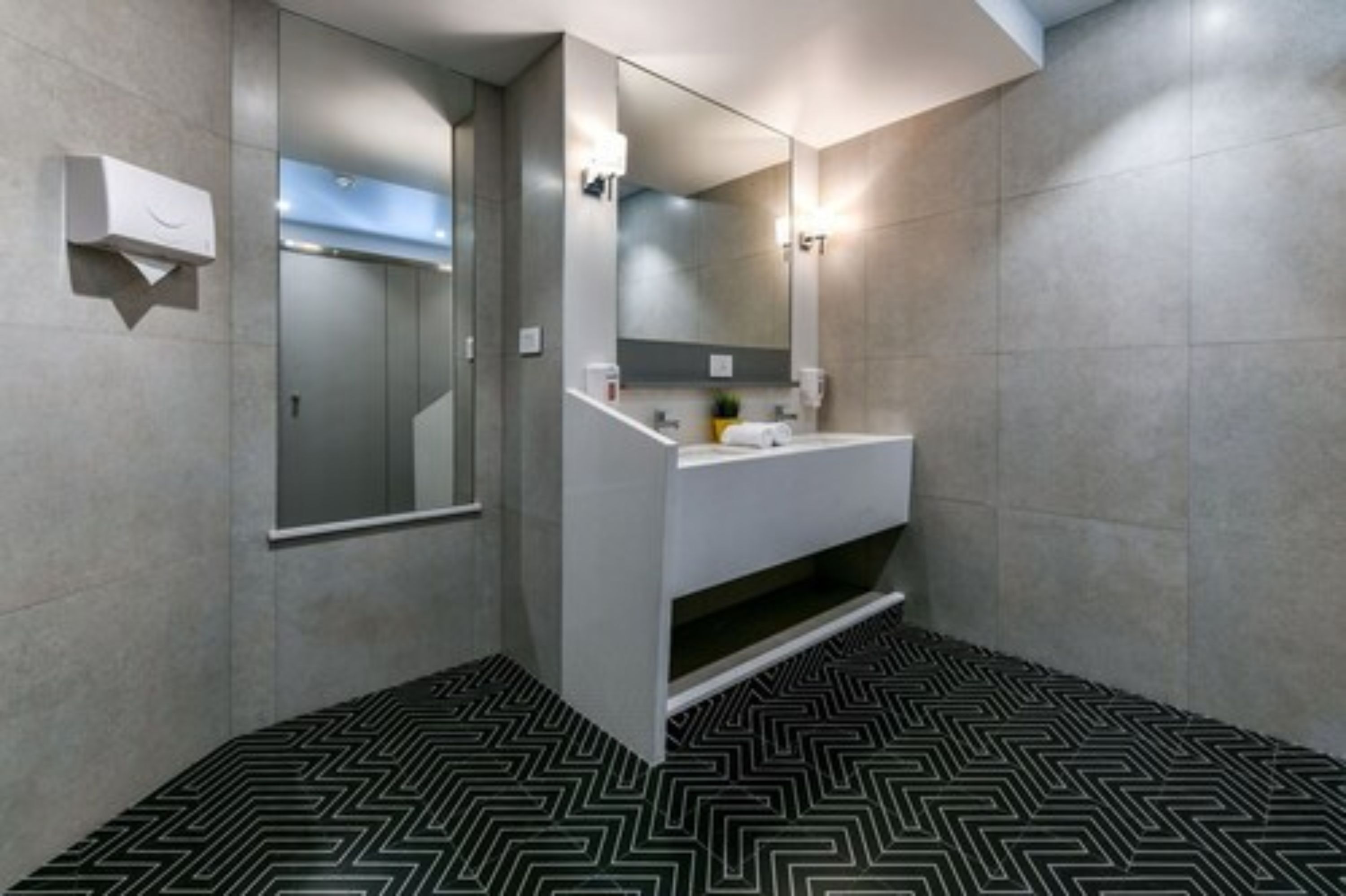 A modern bathroom with a large mirror, a sink, and a patterned floor.