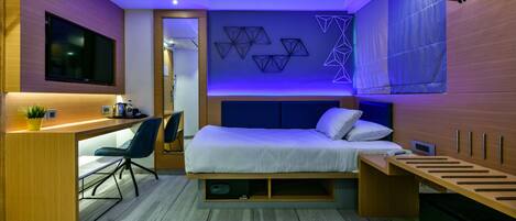 A compact bedroom with a bed, a desk, and a TV.