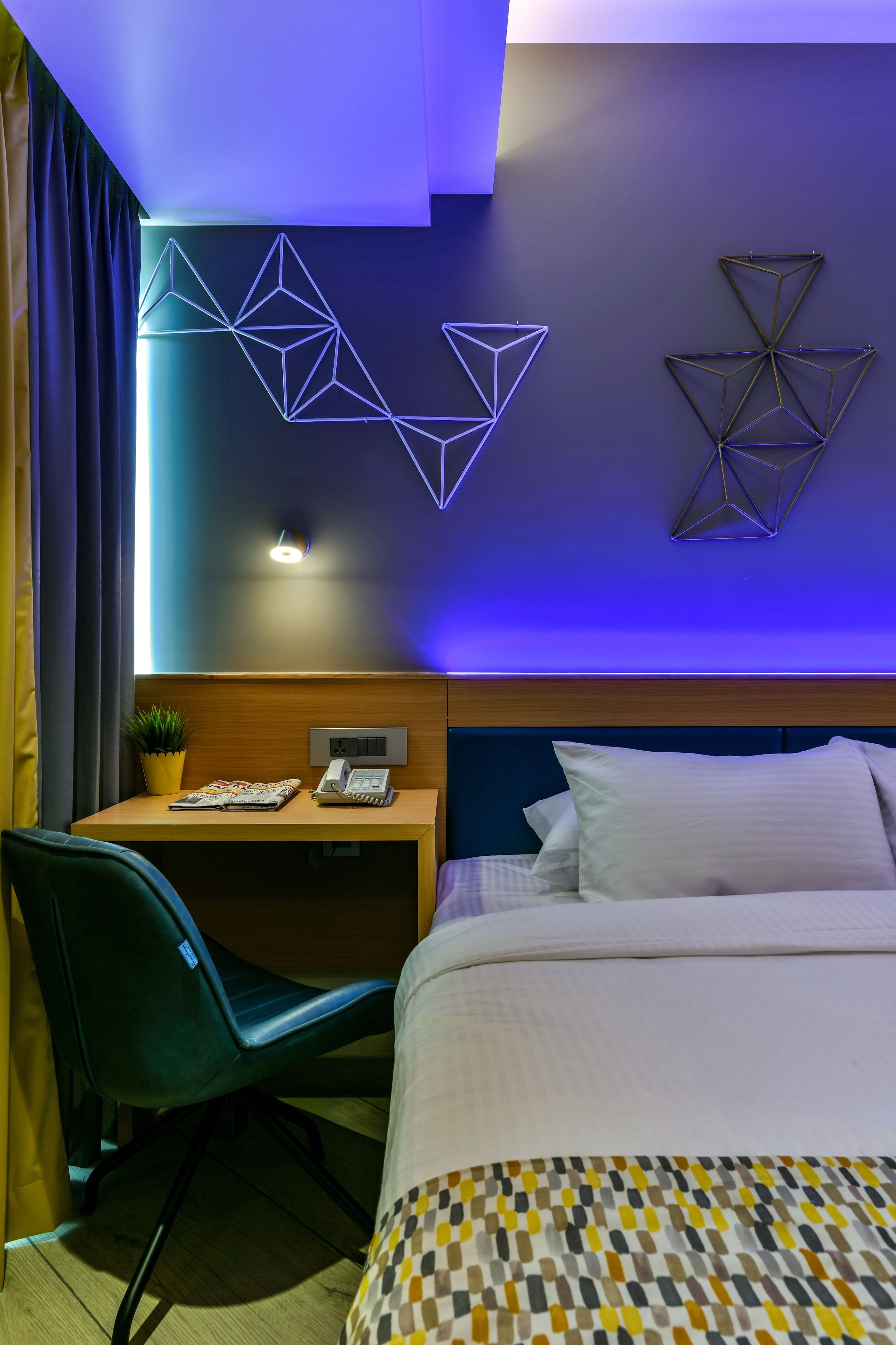 Habitación de hotel con cama, escritorio con silla, teléfono en la pared y arte geométrico en la pared.