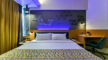 A modern hotel room with a large bed, a desk, a chair, and geometric wall art.