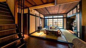 Een traditionele Japanse kamer met tatami vloerbedekking, een lage tafel met kussens, en een schuifdeur naar een tuin.