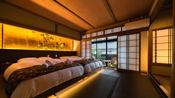 Een traditionele Japanse kamer met tatami vloeren, een groot bed met veel kussens, een schuifdeur van papier en uitzicht op groen.