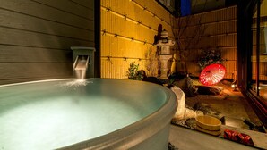 Een hottub met een stenen constructie en een rode parasol in een tuin.