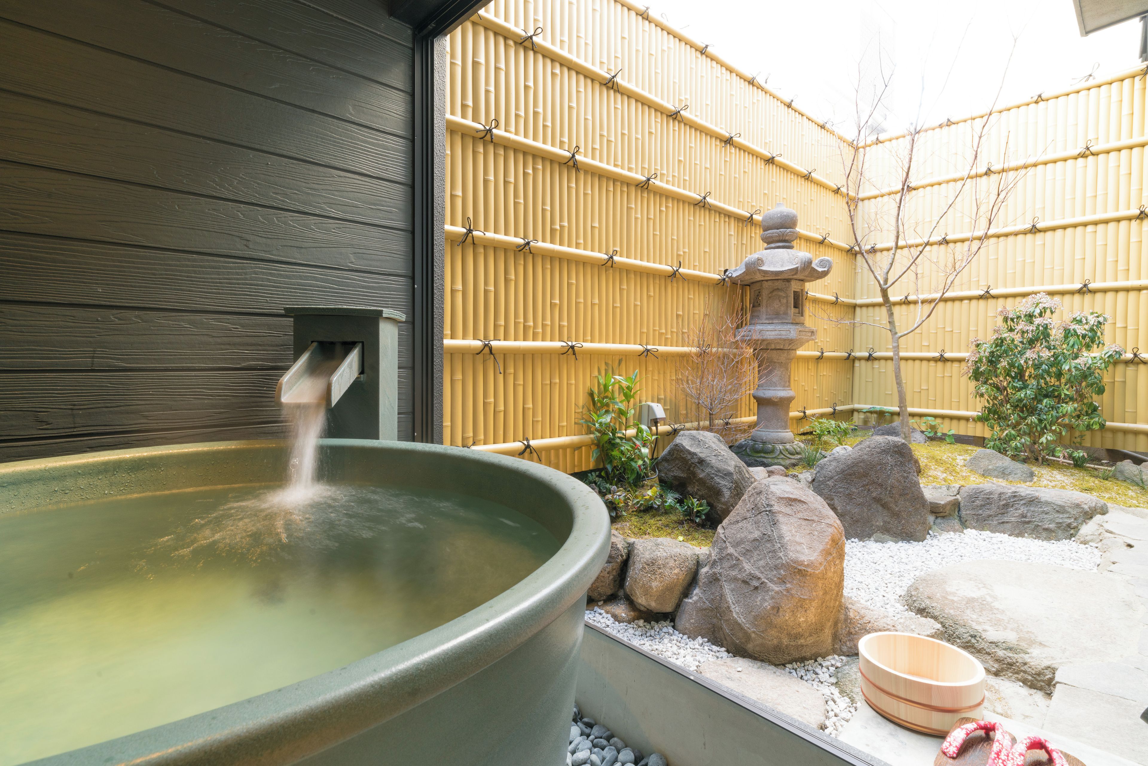 A traditional Japanese onsen with a stone basin, a wooden fence, and a stone lantern.