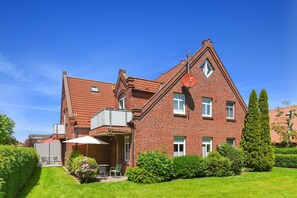 Une maison en briques rouges, avec un toit en pente, une antenne parabolique et une petite terrasse équipée de chaises et d’une table.