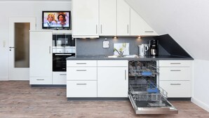 Una cocina moderna con armarios blancos, lavavajillas, cafetera y un televisor que muestra personajes animados.