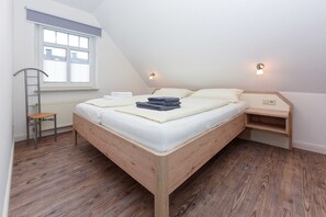 Une chambre à coucher avec un lit en bois, un petit bureau, une chaise et une fenêtre avec des stores.