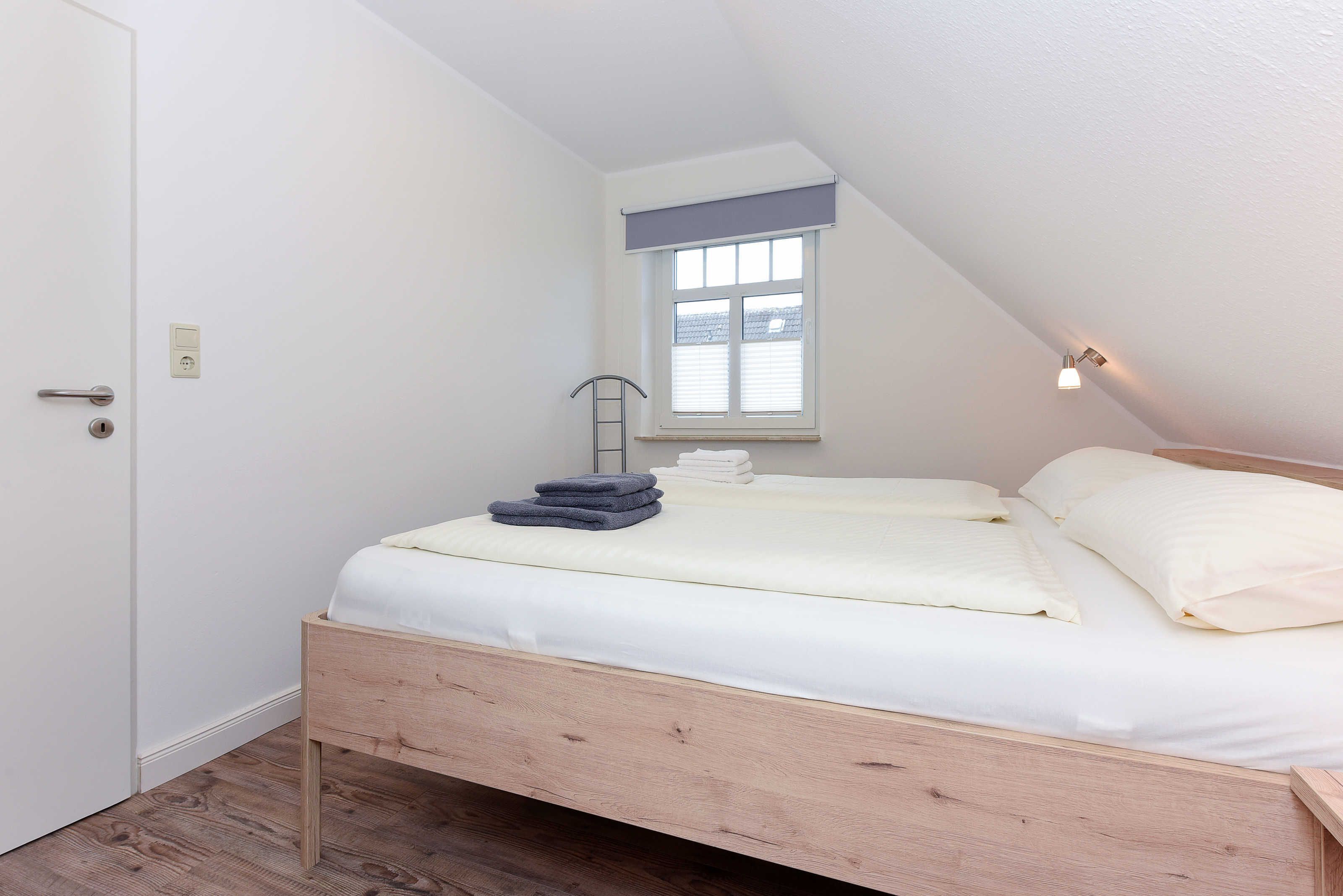 A bedroom with a wooden bed, a window with blinds, a door, and a wall-mounted light fixture.