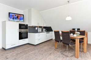 Une cuisine moderne avec des meubles blancs, un four à micro-ondes et un coin repas comprenant une table et des chaises.