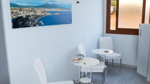 A small, bright room with a large window, a table with chairs, and a wall-mounted picture. - B&B Isole (Naples)