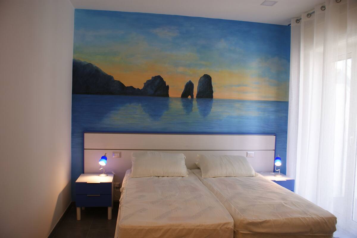 Ein Schlafzimmer mit einem Bett, zwei Nachttischen und einem Gemälde einer Küstenlandschaft an der Wand.
