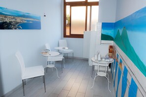 A room with a large window, white chairs, a small table with books, and a painting of a landscape. - B&B Isole (Naples)