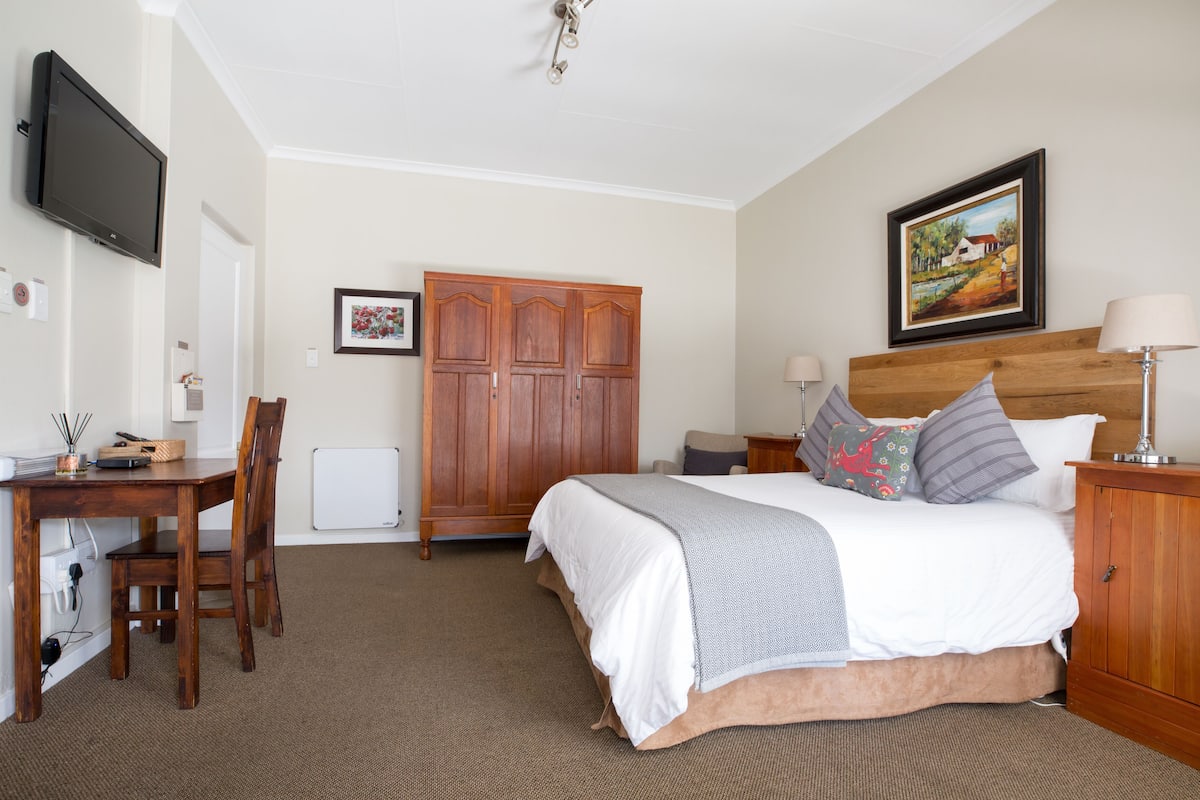 A bedroom with a bed, bedside tables, a desk, a chair, a wardrobe, and a television.