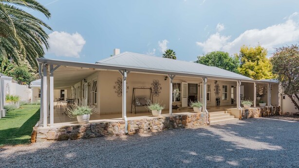 Une maison à deux étages avec un porche couvert, des fondations en pierre et des plantes en pot.