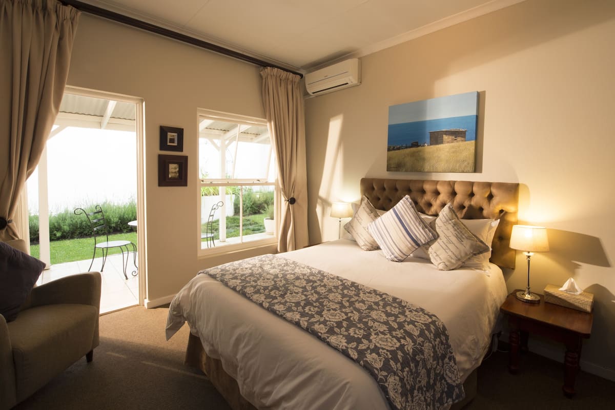 A bedroom with a large bed, a bedside table with a lamp, a chair, and a view of the outdoors through a glass door.