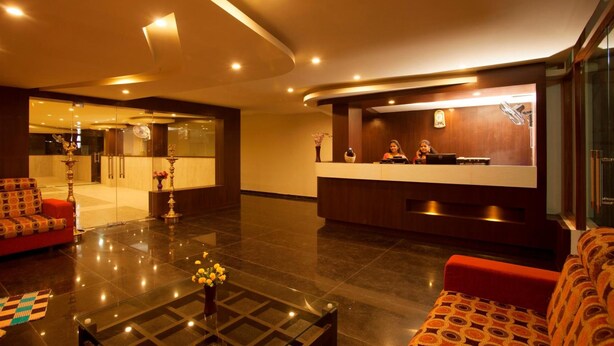 Un vestíbulo de hotel con mostrador de recepción, zona de estar y una mesa de centro de cristal con flores.