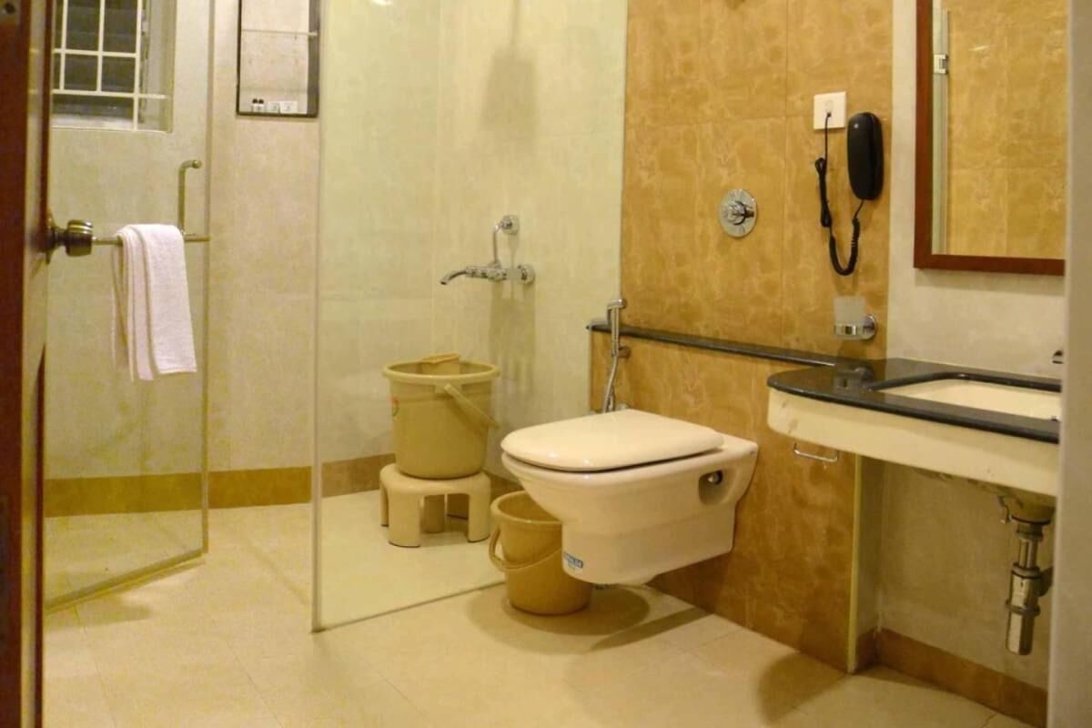 A bathroom with a toilet, sink, and shower. There is a telephone and a mirror on the wall.