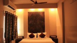 Habitación de hotel con cama, ventilador de techo, mesita de noche y aire acondicionado instalado en la pared.
