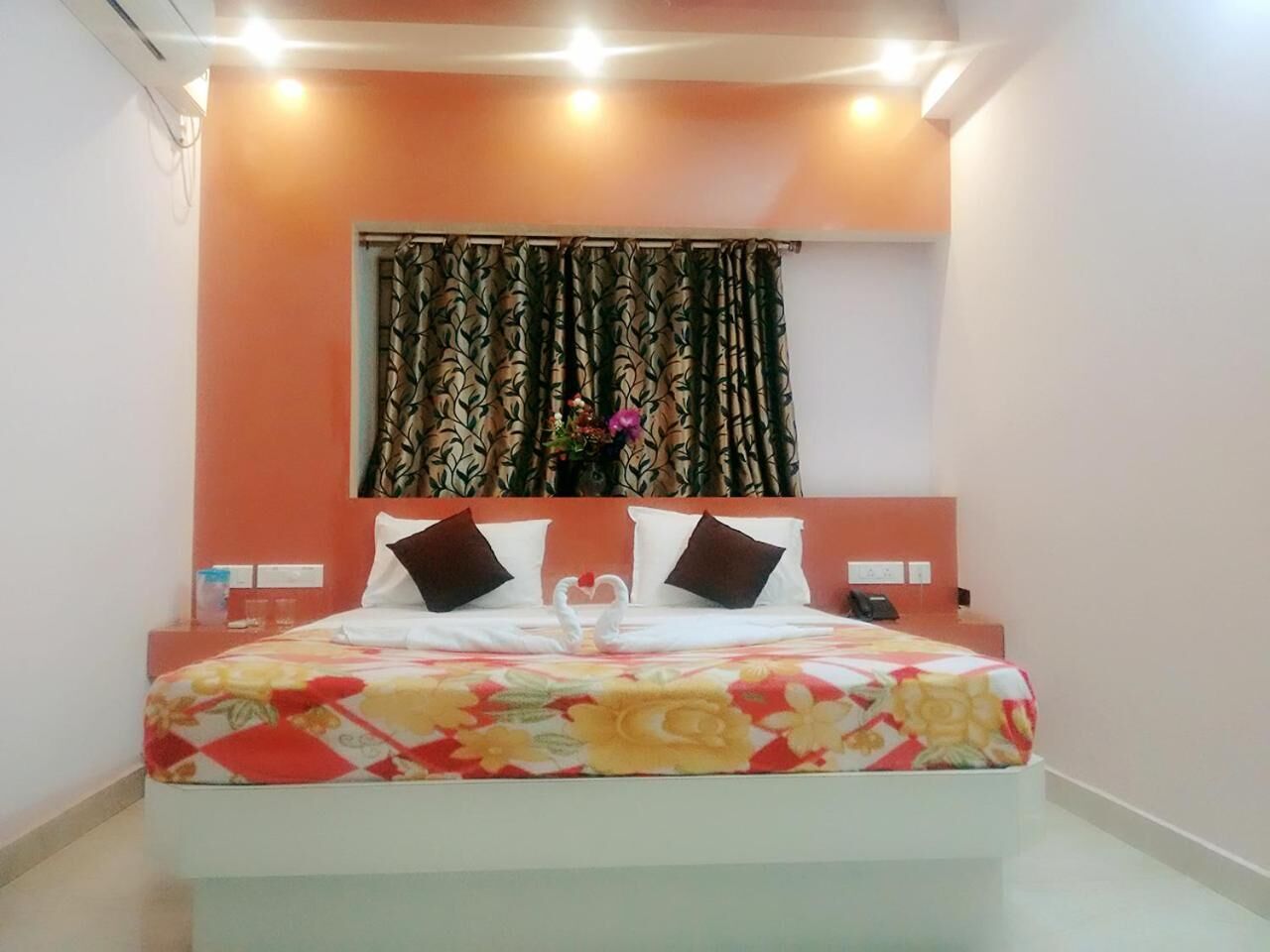 A neatly made bed with a floral bedspread, two pillows, and a vase with flowers on the nightstand.