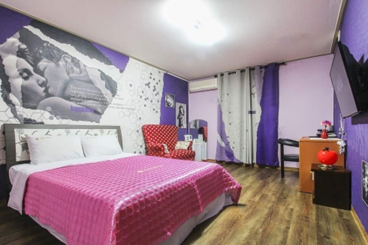 A bedroom with a bed, a red chair, a desk, a television, and a wall with a poster.
