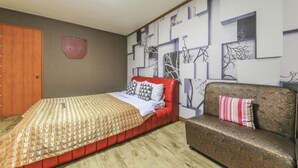 Un dormitorio con cama, sofá, puerta de madera y una pared decorada con arte abstracto.