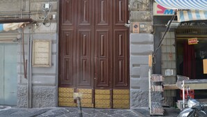 Una puerta de madera grande con una placa, un portón de metal y una tienda con toldo a rayas.