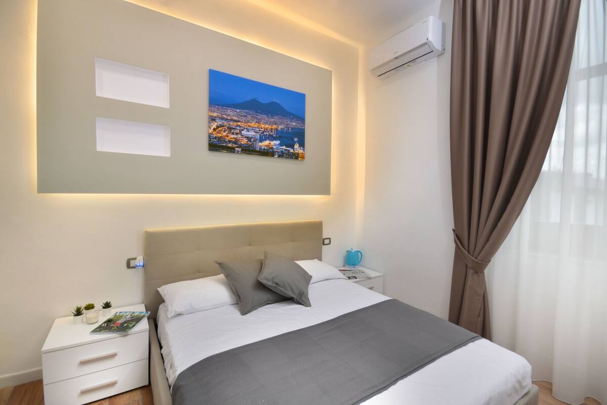 A neatly arranged bedroom with a bed, bedside tables, a nightstand, and a wall-mounted air conditioner.