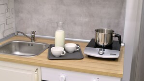 Una cocina con un lavamanos, una estufa y una tetera, además de dos tazas blancas sobre una bandeja.