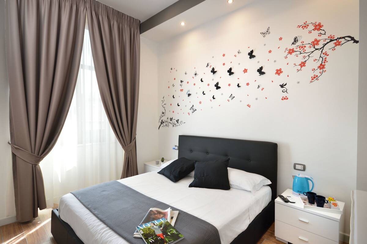 A neatly made bed with a white and gray bedspread, black pillows, and a remote control on a bedside table.