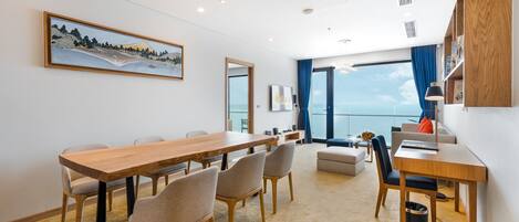 Una habitación de hotel moderna con una mesa de comedor de madera, asientos cómodos, un ventanal con vistas y una obra de arte colgada.