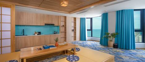 Une chambre d’hôtel moderne avec un plafond en bois, une grande fenêtre ornée de rideaux bleus, une table à manger en bois et un tapis bleu à motifs.