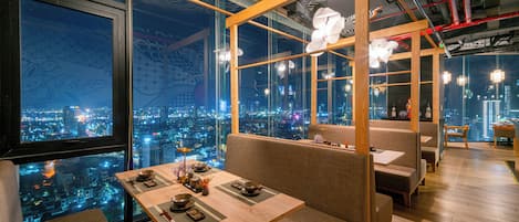 A restaurant with a city view, wooden furniture, and hanging paper lanterns.