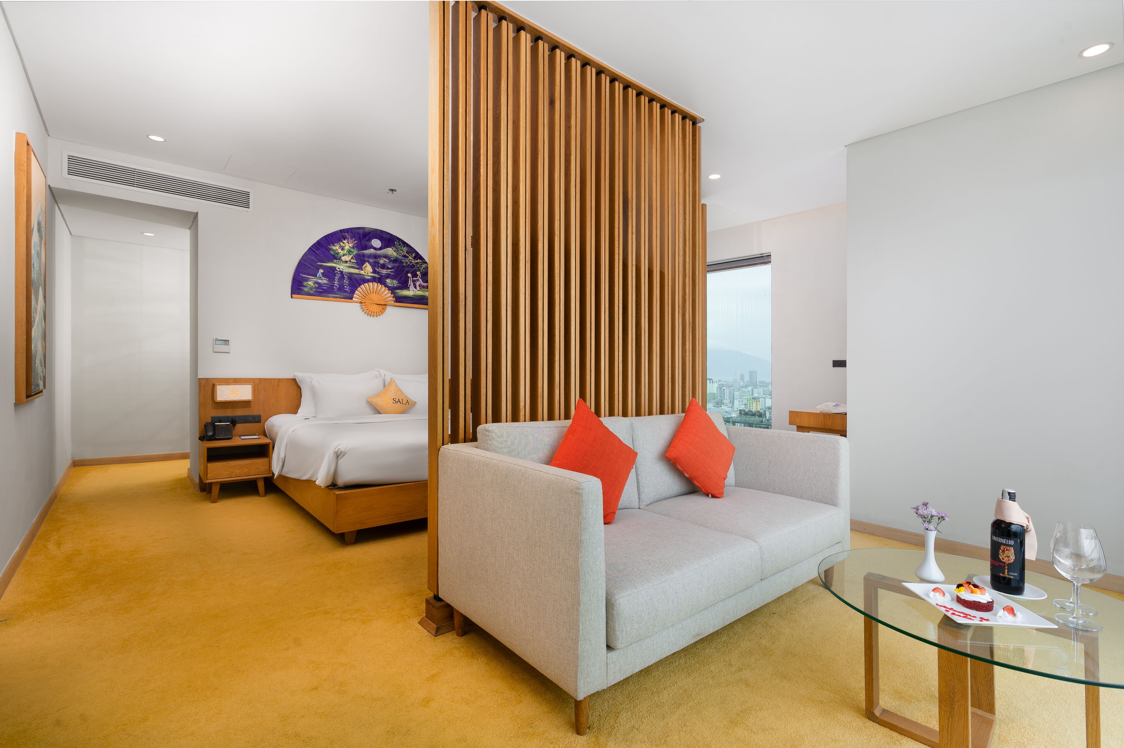 A hotel room with a bed, a sofa, a glass coffee table, and a city view.