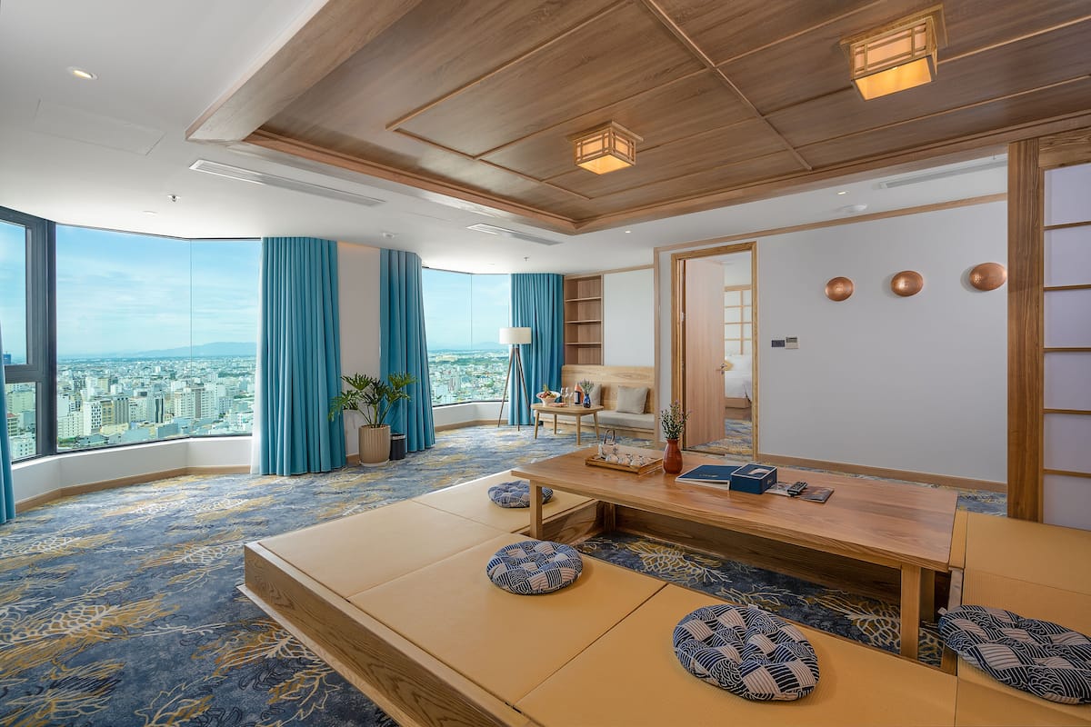 A modern hotel room with a large window offering a city view, a wooden ceiling, and a traditional Japanese tatami mat seating area.