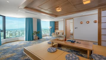 A modern hotel room with a large window offering a city view, a wooden ceiling, and a traditional Japanese tatami mat seating area.
