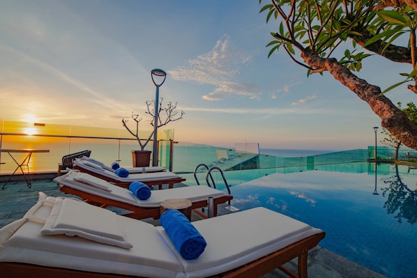 Relax by the infinity pool overlooking the ocean with comfortable sun loungers and a glass railing.
