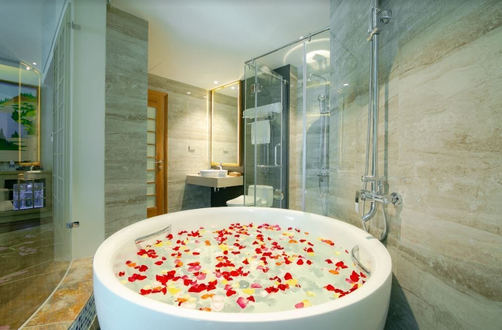 Un baño moderno con una bañera grande llena de pétalos de rosa, una cabina de ducha con paredes de vidrio y un mostrador de baño visible.