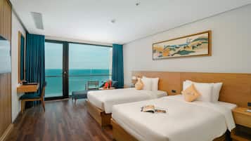 Une chambre d’hôtel avec deux lits, un bureau, une chaise et une grande fenêtre donnant sur la mer.