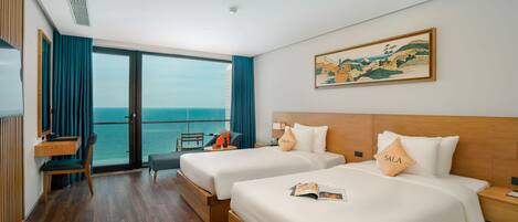 Habitación de hotel con dos camas, un escritorio, una silla y un amplio ventanal con vista al mar.