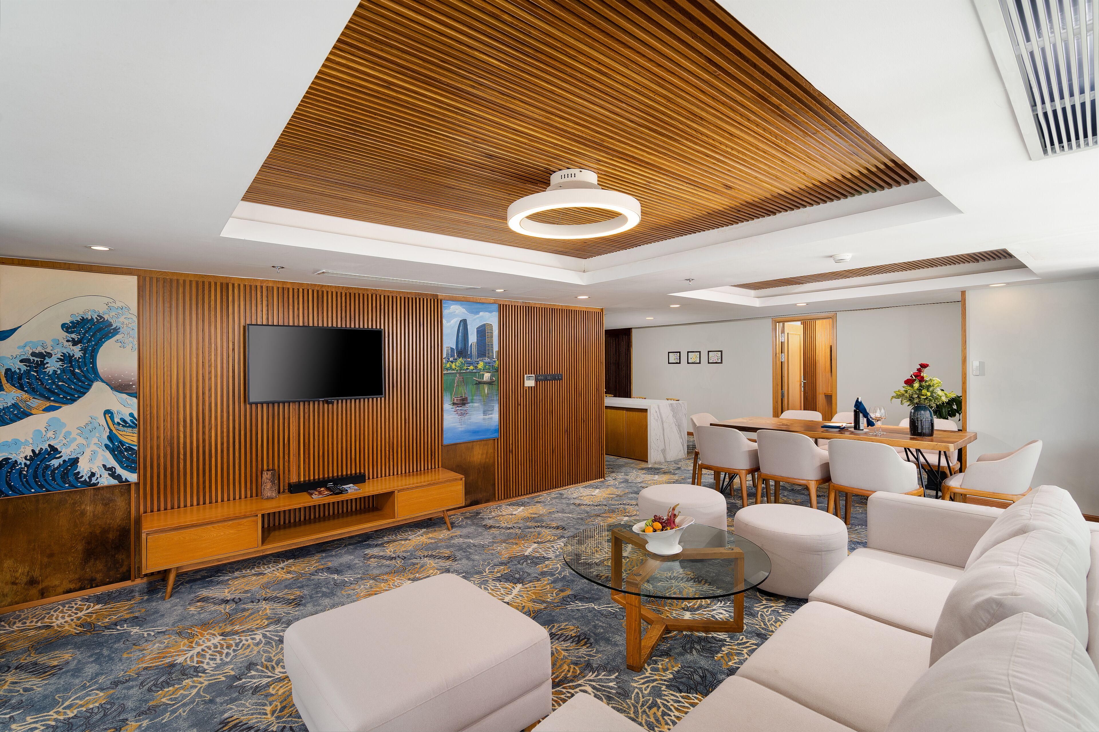 Una habitación de hotel moderna con techo de madera, televisor de pantalla plana, zona de comedor y un cuadro grande en la pared.