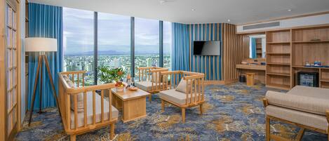 A spacious room with large windows, a flat-screen TV, wooden furniture, and a city view.