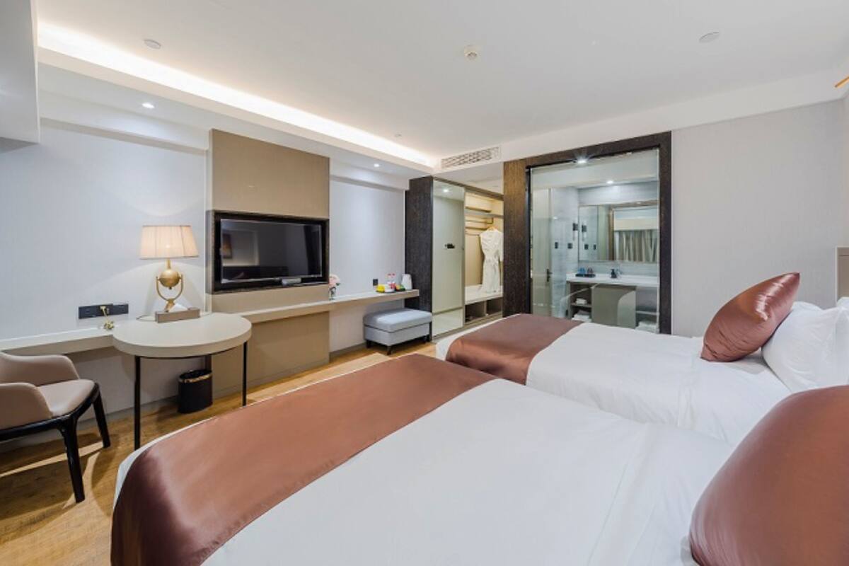 Ein Hotelzimmer mit zwei Betten, einem Schreibtisch, einem Fernseher und einem Spiegel.