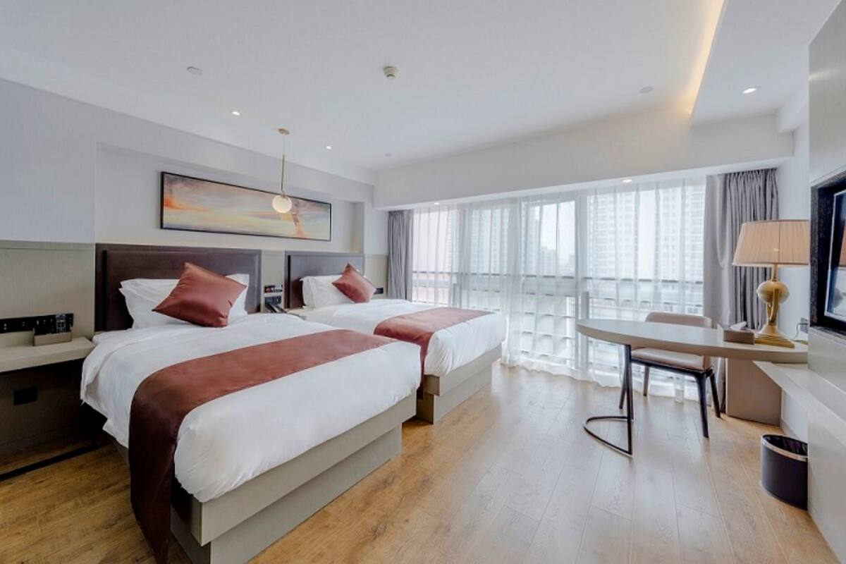 Ein Hotelzimmer mit zwei Betten, einem Schreibtisch und einem großen Fenster mit Vorhängen.