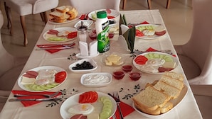 A dining area with a long table set for breakfast, surrounded by white upholstered chairs. - Eleganti (Batumi)