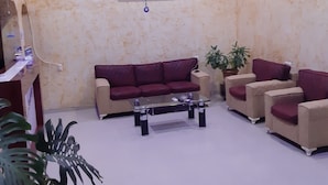 A living room with a beige sofa, a glass coffee table, and two armchairs. There is a painting on the wall and a ceiling light fixture. - Eleganti (Batumi)