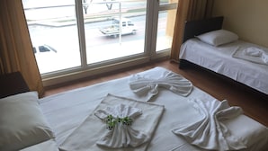 A hotel room with two beds, a large window with a view of the street, and a neatly made bed with towels arranged in a bow shape. - Eleganti (Batumi)