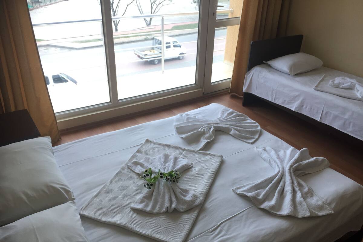 A hotel room with two beds, a large window with a view of the street, and a neatly made bed with towels arranged in a bow shape.