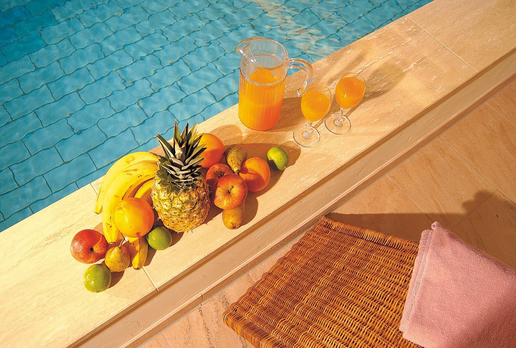 Een tafel bij het zwembad met fruit, een karaf sinaasappelsap en twee glazen.