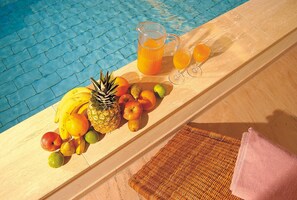 A poolside table with fruits, a pitcher of orange juice, and two glasses. - Hotel Klumpp (Baiersbronn)